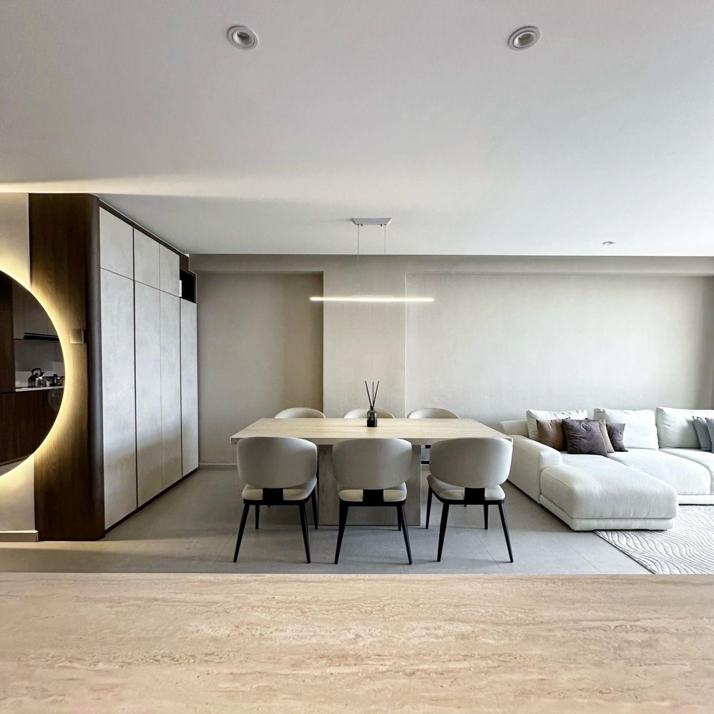 Dining table beside a backlit round mirror and a cream sofa